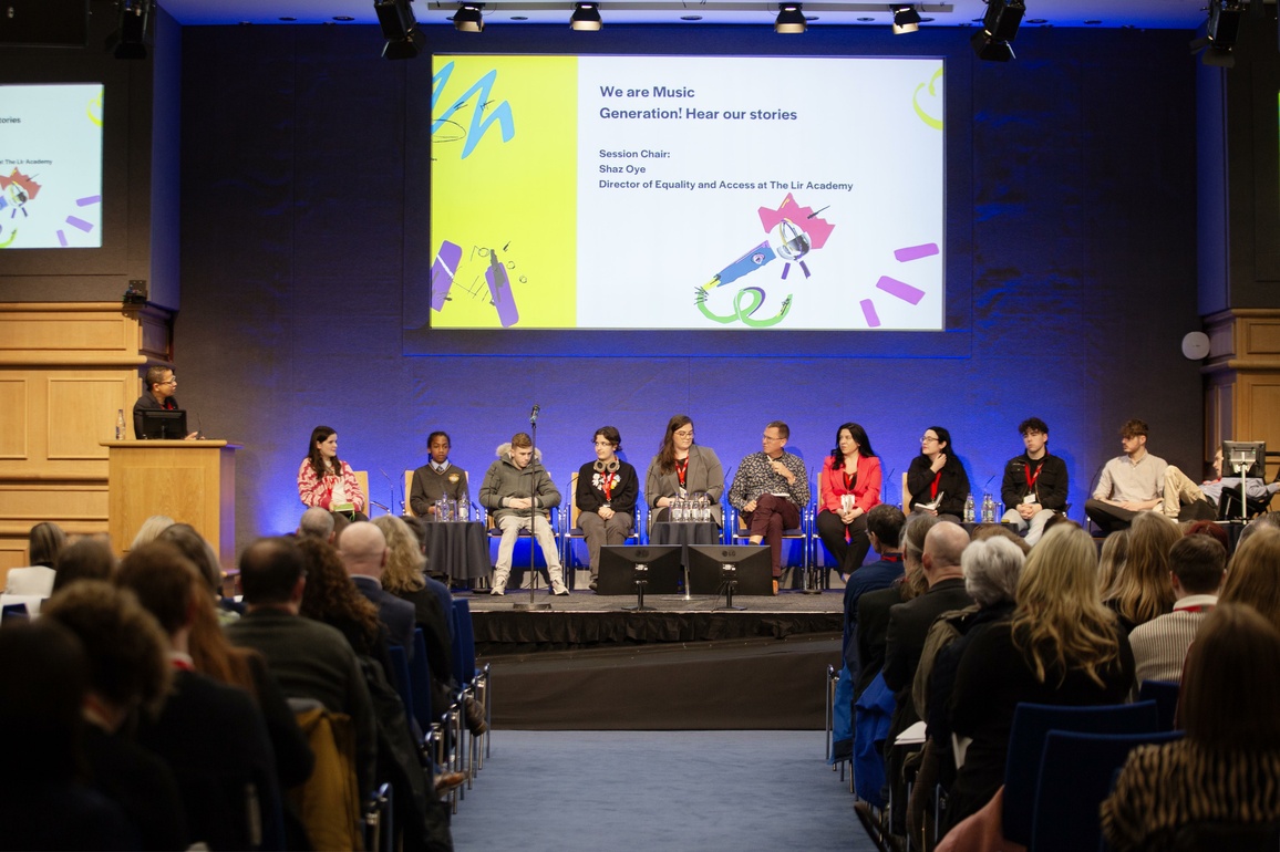 4 young panellists and 5 adult panellists sitting on stage with chair standing to left of stage