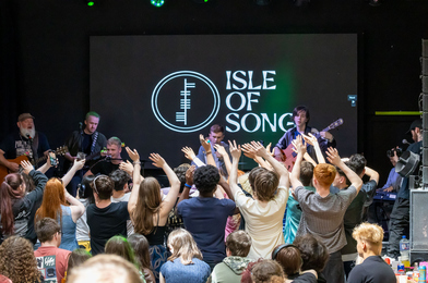 Audience members with their hands in the air in front of a stage with a young band performing.