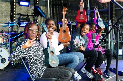 Group of young musician sitting on a stage smiling and holding their ukuleles in the air